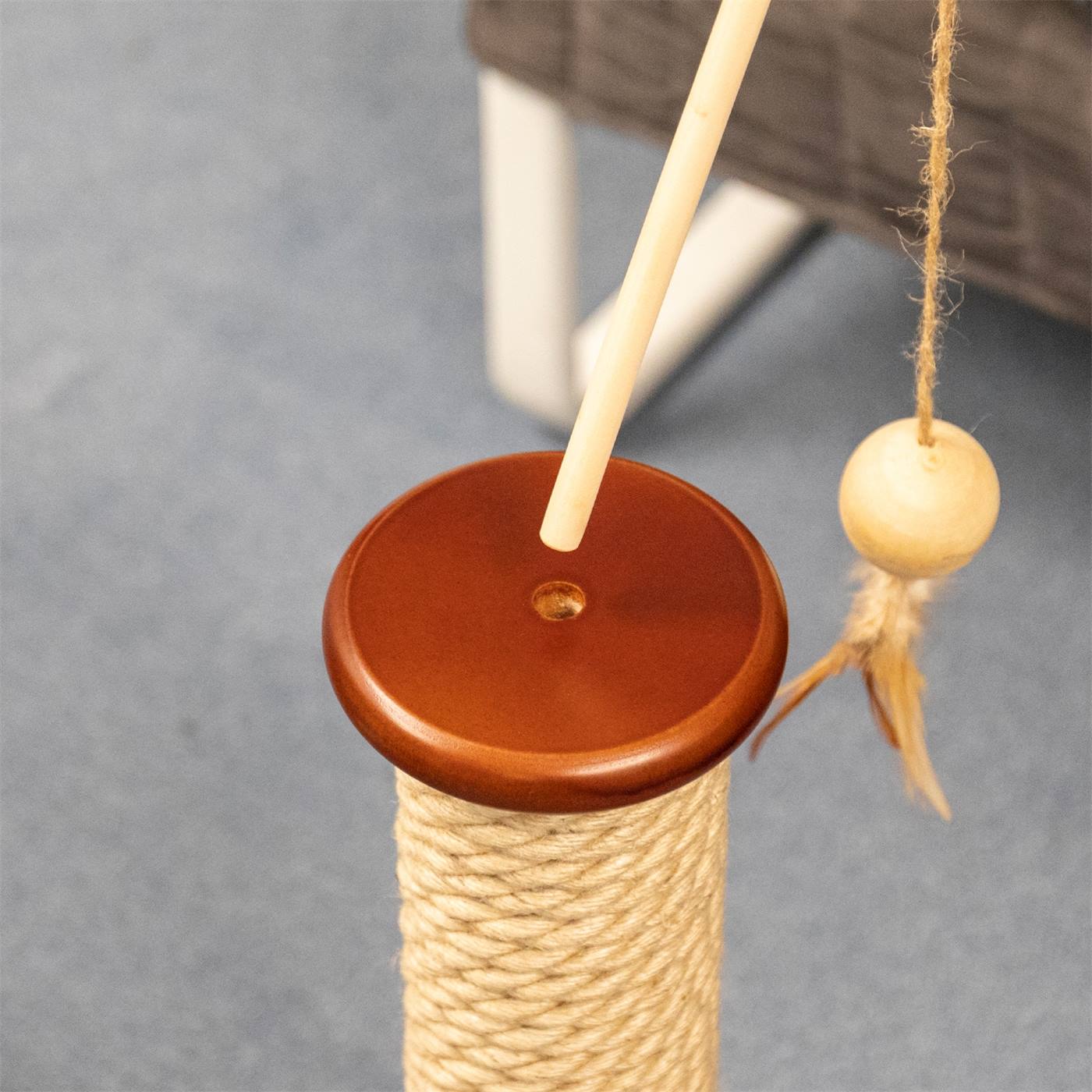 Double-cliquez pour agrandir Une main tient le jouet à gratter "Kingu" de VOSS.pet Jouet pour chats, composé d'un bâton en bois avec une ficelle attachée à une balle en bois et des plumes, sur un fond blanc.